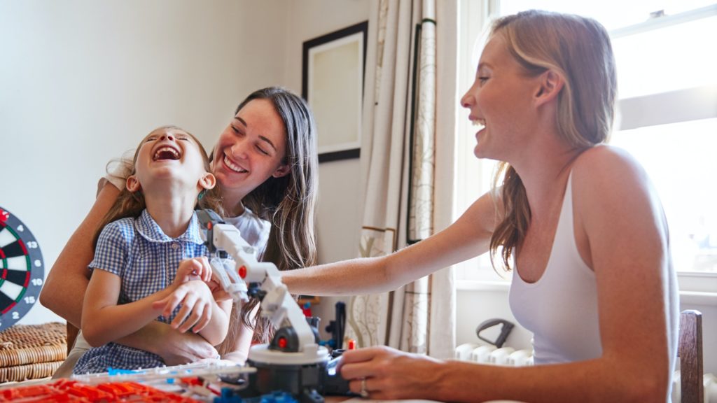 Same Sex Female Couple Making Robot From Kit With Daughter In Bedroom At Home Together